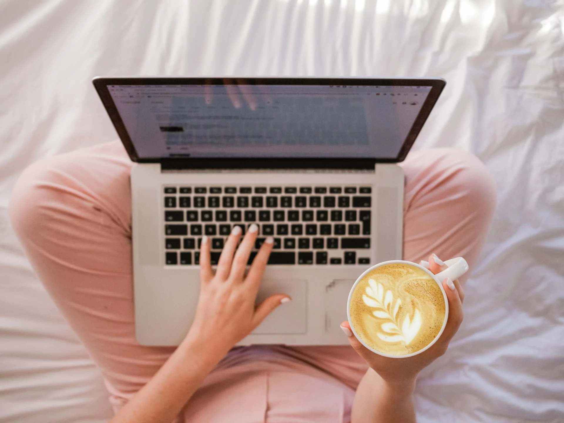 Ordinateur portable et tasse de café posés sur un lit, en télétravail